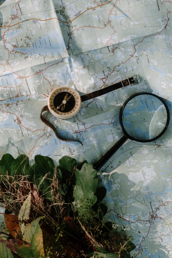A compass and magnifying glass on a map with leaves. Perfect for travel or exploration themes.